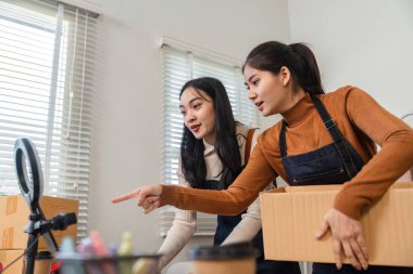 İki genç kadın çevrimiçi giyim sektöründe iş birliği yapıyor, envanterlerini yönetirken ve ürünlerini sergilerken stratejileri tartışıyorlar..