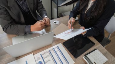 Modern bir ofiste finansal belgeleri ve verileri analiz eden, takım çalışmasını ve stratejik planlamayı sergileyen iş adamlarının genel bir bakış açısı.