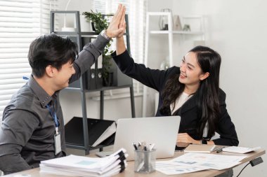 İki iş adamı, modern ofis ortamında takım çalışmalarını ve başarılarını kutlamak için beşlik çakıyor..
