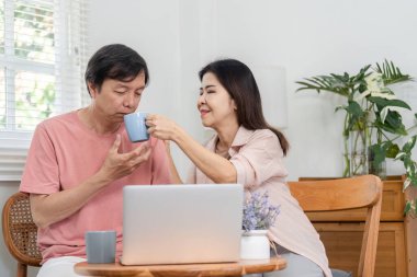 Evde dizüstü bilgisayarda çalışırken içkilerini paylaşan olgun bir çift rahat bir ortamda bağlantının ve desteğin tadını çıkarıyor..