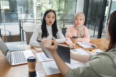 Modern bir ofisteki kadınlar finansal belgeler üzerinde işbirliği yapıyor, stratejileri tartışıyor ve profesyonel bir ortamda görüşleri paylaşıyorlar.