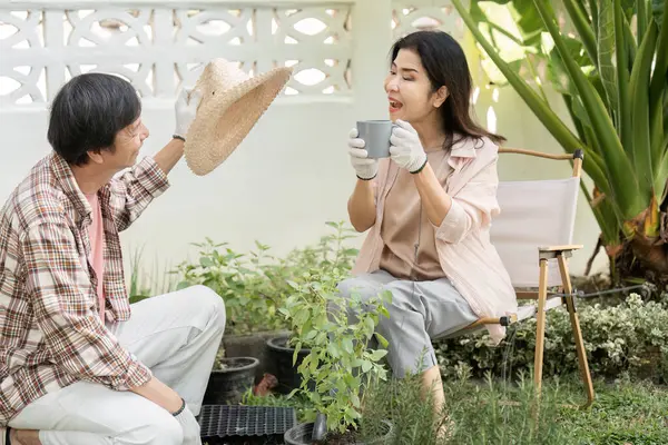 Bahçelerinde çeşitli bir çift, neşeli bir an paylaşıyorlar. Biri elinde bir hasır şapka, diğeri ise bitkilerle çevrili kahveyi yudumluyor..