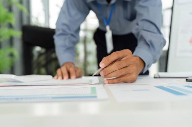Bir işadamı, modern bir ofiste ayrıntılı ve stratejik planlamalara dikkat ettiğini gösteren mali raporları yakından inceler..