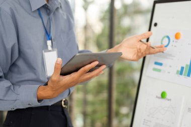 Bir şirket çalışanı tablet tutar ve dijital bir panoya doğru hareket eder. Veri içgörüleri ve analizleri gösterir..