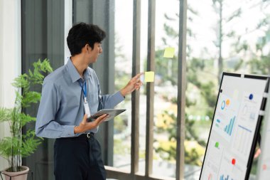 Uzaktan çalışma stratejisi oturumunda fikirler sunan odaklanmış bir işadamı, dijital tablet ve beyin fırtınası için yapışkan notlar kullanıyor.