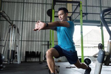 Genç bir adam spor salonunda bir hamle egzersizi yapıyor, genel sağlık eğitimi için güç ve uygunluk eğitimini vurguluyor..