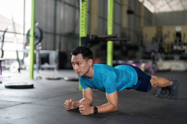 Odaklanmış bir adam, iyi donanımlı bir spor salonunda kalas egzersizi yapar, güç ve kararlılık gösterir..