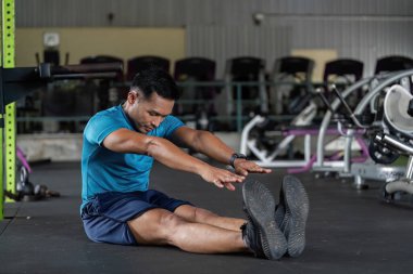 Spor salonunda esneme egzersizi yapan bir adam esneklik ve zindeliğe odaklanıyor. Atmosfer enerjik ve motive edici..