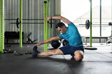 Formda bir adam spor salonunda esneklik ve sağlığa odaklanarak yan esneme hareketleri yapar. Sağlık ve zindelik temaları için ideal.