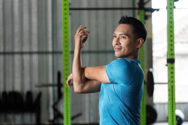 Spor salonunda kol esneme hareketleri yapan bir adam spor salonundaki esnekliğin önemini gösterir..