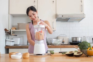 Genç bir kadın, modern bir mutfakta, sağlık ve sağlığa odaklanarak meyve suyu karıştırıyor..