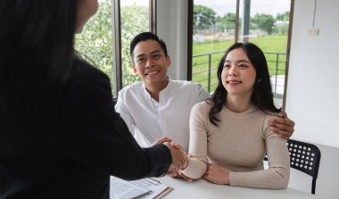 Neşeli bir çift bir emlakçıyla emlak satış sözleşmesini sonuçlandırır. Ev satın alma yolculuklarında yeni bir başlangıcı sembolize eder..