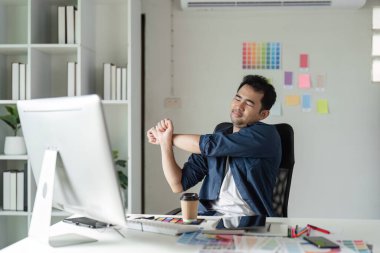 Genç bir tasarımcı, modern ofis ortamında yaratıcı aletlerle çevrili bir masada çalışırken kendini rahatsız hisseder..