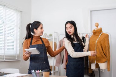 İki kadın girişimci moda stratejilerini tutkuyla tartışarak, online gömlek butik çalışma alanlarında şık kazaklar sunuyorlar..