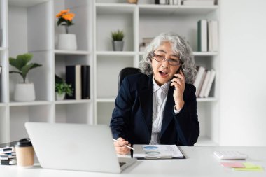 Yaşlı bir iş kadını ofisinde güvenle konuşuyor, liderlik ve yönetim becerilerini gösteriyor..