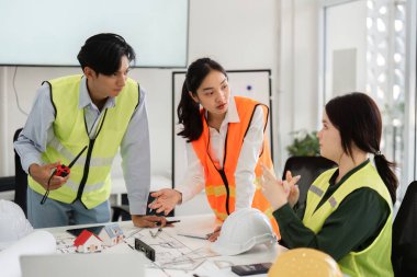 Çeşitli bir inşaat ekibi etkin bir şekilde bina planları, parlak modern ofis ortamında işbirliği ve iletişim hakkında ayrıntılı bir tartışmaya girişti..