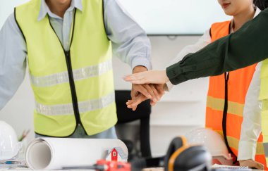 Güvenlik yelekleri içinde işbirlikçi bir inşaat ekibi verimli bir proje planlama toplantısında birlik ve bağlılığı sembolize ederek ellerini birleştiriyor..