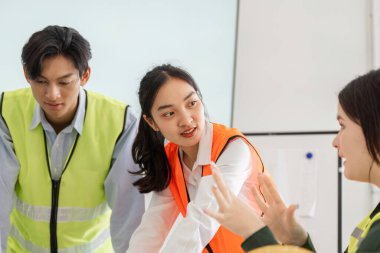 Aralarında güvenlik yelekli bir kadın ve iki erkeğin de yer aldığı bir inşaat profesyonelleri ekibi, ortak bir ortamda proje planları hakkında animasyon tartışmalarına giriştiler..
