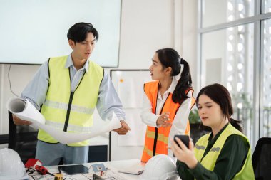 Çağdaş ofis ortamında proje özelliklerini tartışırken, mimari planlarını inceleyen çeşitli bir inşaat ekibi etkili takım çalışması sergiliyor.