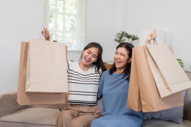 Bir anne ve kızın alışveriş torbalarını kaldırıp sıcak bir oturma odasındaki rahat bir kanepede birlikte sevinçlerini ve heyecanlarını ifade ettikleri canlı bir an..