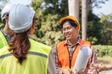 Neşeli bir lojistik mühendisi ve meslektaşları, bir inşaat sahasında projenin kilometre taşlarını tartışıp planlarını gözden geçiriyorlar..
