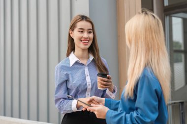 Çağdaş bir ortamda elinde tablet ve kahveyle gülümseyen ve fikir alışverişinde bulunan iki farklı kadın..