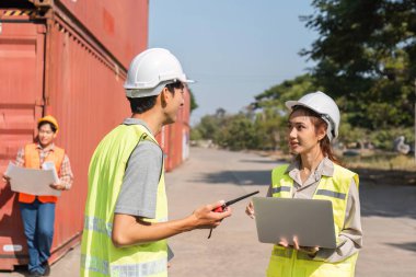 Proje detayları üzerinde çalışan üç inşaat işçisi, bir erkek denetçi ve kadın mühendis konteynerlerin önünde planları tartışıyorlar..