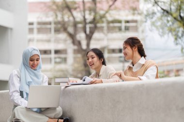 Üç farklı kız öğrenci bir üniversitede birlikte çalışıyor, notlarını paylaşırken dizüstü bilgisayar kullanıyorlar ve birlikte ders çalışmaktan zevk alıyorlar..