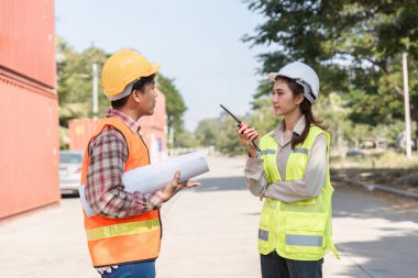 Bir lojistik mühendisi ve proje yöneticisi, inşaat sahasında iletişim için bir telsiz kullanarak proje sorunları hakkında ayrıntılı bir tartışmaya girişirler..