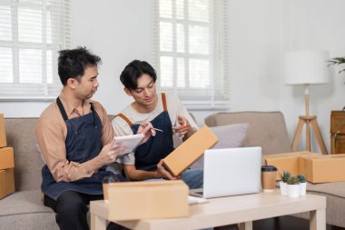 İnternette iş birliği yapan iki adam şık oturma odalarında paketlenmiş kutularla birlikte satılık eşyaları gözden geçiriyorlar..