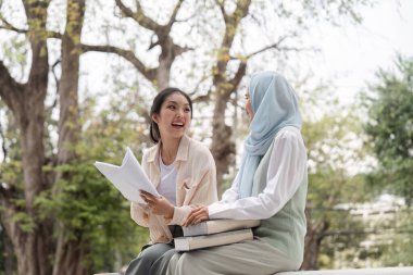 Çeşitli kız öğrenciler, canlı bir tartışma içindeler, sakin bir üniversite parkında oturmuş, kitap ve notlar tutuyorlar, gülümsemelerini ve fikirlerini paylaşıyorlar..