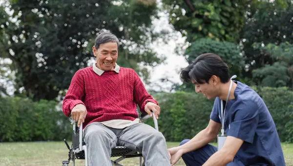 Kırmızı kazaklı yaşlı bir adam, huzurlu bir bahçede şefkatli bir sağlık görevlisiyle, dostluğu ve empatiyi simgeleyen neşeli bir anı paylaşıyor..