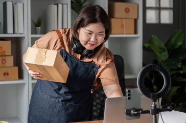 Kulaklık takan bir e-ticaret girişimcisi, ev ofisinde bir sevkiyat hazırlıyor, organizasyon becerilerini ve online perakende işine olan bağlılığını vurguluyor..