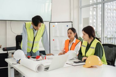 Aralarında mimarlar ve mühendislerin de yer aldığı çeşitli bir inşaat ekibi, parlak, modern bir ofiste mimari planlar ve tasarımları yoğun bir şekilde tartışıyor..