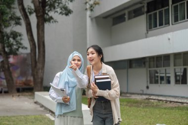 İki farklı üniversite öğrencisi neşeli bir anı paylaşıyor ve kampüste yürürken gülüyorlar, arkadaşlıklarını ve arkadaşlıklarını vurguluyorlar..