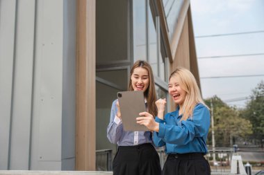 Çağdaş bir ortamda açık havada tablete bakarken iki farklı kadın mutlulukla başarıyı kutluyor..