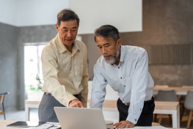 İki kıdemli iş adamı, bir dizüstü bilgisayardaki finansal verileri analiz ederken çağdaş bir ofiste önemli ayrıntılara dikkat çekiyorlar..