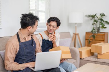 İki adam rahat bir sohbeti paylaşıyor. Biri elinde kahve fincanı, diğeri de rahat oturma odalarındaki kutuların arasında dizüstü bilgisayarla çalışıyor..