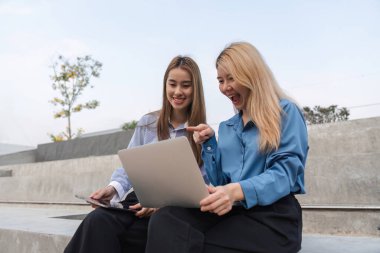 Dışarıdaki iki iş kadını, verileri tartışırken ve incelerken heyecanlı bir şekilde dizüstü bilgisayarı işaret ederek, işbirlikçi bir ortamda coşku gösteriyorlar..