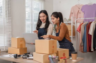 İki hevesli kadın, çevrimiçi satıcı, hevesle dizüstü bilgisayarlarını gösteriyorlar, en son siparişlerini, konforlu bir giyim mağazasında nakliye kutularının arasında tartışıyorlar..