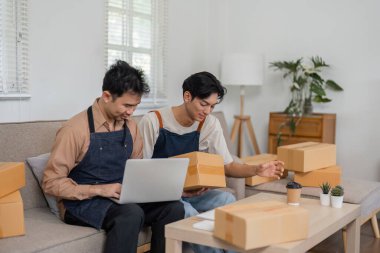İki dost canlısı sosyal medya pazarlamacısı ürün detaylarıyla ilgili bir tartışmaya giriştiler, biri dizüstü bilgisayar, diğeri ise paket taşıyordu, modern ev ofislerinde kutularla doluydu..