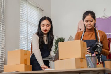 Çevrimiçi siparişleri düzenleyen ve şık butik çalışma alanlarında sevkiyat yapmak için dizüstü bilgisayar kullanan farklı bir çift..