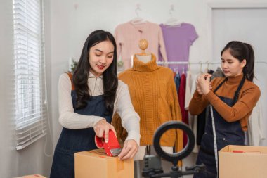Kutuları mühürlemek ve nakliyatları hazırlamak için bant kullanan iki farklı perakende işçisi, canlı bir perakende ortamda kıyafet düzenlerken....