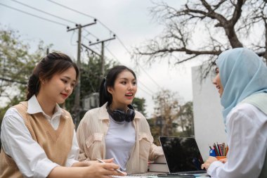 Üniversite öğrencilerinden oluşan çeşitli bir grup, akademik projeler üzerinde dizüstü bilgisayar ve defterlerle ciddi bir tartışmaya giriştiler..