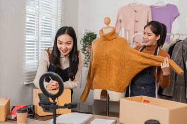 Manken üzerinde şık bir süveter sunan iki farklı perakende işçisi, bir mağazada çevrimiçi satışlar için envanter ve kayıt işletiyorlar..