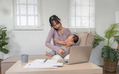 Bebeğini evde rahat bir ortamda nazikçe tutarken telefonda konuşan çok görevli bir anne..