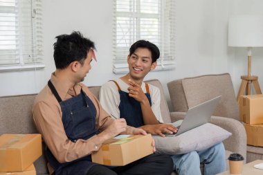 Neşeli bir LGBT çifti çevrimiçi işleri, eşyaları paketlemek ve sıcak oturma odalarında beyin fırtınası yapmak hakkında sohbet ediyorlar..