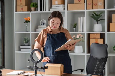 Kendine güvenen genç bir kadın ürün satışlarını modern ofisinden canlı olarak sunuyor, siparişleri kontrol ediyor ve girişimci ruhunu sergiliyor..
