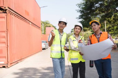Bir mühendis, bir proje yöneticisi ve bir işçiden oluşan çeşitli bir inşaat ekibi, çalışkan bir inşaat sahasında proje planları ve planlarını tartışıyor..