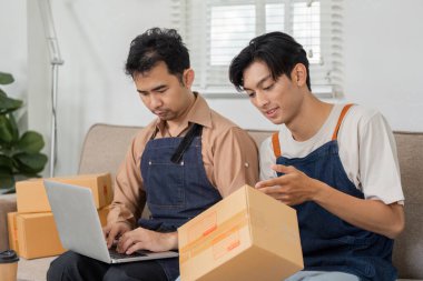 İki teslimat uzmanı, biri dizüstü bilgisayarda diğeri paketle ilgileniyor, paketlerle dolu rahat bir çalışma ortamında etkili bir şekilde işbirliği yapıyorlar..